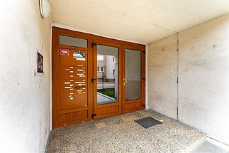 Vstupní hala s dlažbou a prosklenými dveřmi, moderní schránky a jednoduchá omítka, působící udržovaně a čistě