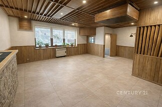 Světlý obývací pokoj s dlažbou, dřevěným obložením a velkými okny, nabízí moderní design a prostorný interiér.