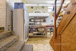 Funkční kuchyně s dlažbou a nerezovými spotřebiči, vybavená velkým odsávačem par a otevřenými regály, historický styl.