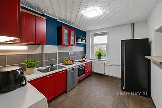 Moderní kuchyň s parketovou podlahou, červenými skříňkami a velkým oknem. Nabízí dostatek úložného prostoru a spotřebiče z nerezové oceli.