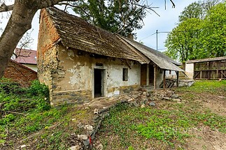 Starý venkovský dům s kamennou fasádou, dřevěnou střechou a potřebou rekonstrukce, nachází se na prostorném pozemku obklopeném zelení.