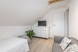 Světlý podkrovní pokoj s dřevěnou podlahou, bílou komodou a moderní pohovkou, ideální prostor pro relaxaci.