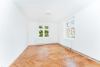 Světlý obývací pokoj s parketovou podlahou, velkými okny a moderním designem, ideální pro vytvoření útulného prostředí.