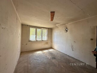 Prostorný pokoj s parketovou podlahou, velkým oknem a potřebou rekonstrukce, nabízející potenciál pro moderní úpravy.