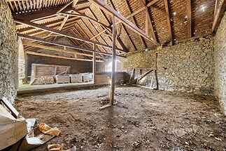 Prostorná stodola s kamennými zdmi, odkrytou dřevěnou střechou a velkým obloukovým oknem, ideální pro rekonstrukci a investici.
