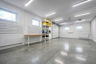 Moderní garáž s betonovou podlahou, vestavěnými policemi a úložnými prostory, světlé díky velkým oknům a dobrému osvětlení.