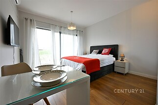 Světlý pokoj s parketovou podlahou, velká okna poskytují dostatek světla, moderní nábytek dodává elegantní vzhled.