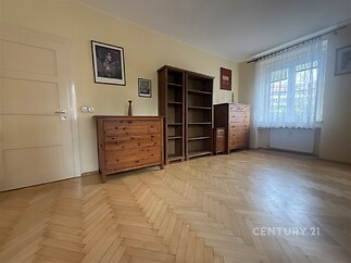 Prázdný pokoj s parketovou podlahou, velkými okny a dřevěným nábytkem, ideální pro rekonstrukci nebo jako světlý obývací prostor.