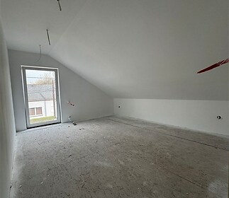 Podkrovní místnost, světlá a prostorná, připravená na dokončení, s velkým oknem a šikmým stropem, ideální pro moderní úpravy