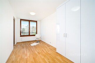 Světlý pokoj s parketovou podlahou, velkými okny a bílými vestavěnými skříněmi, moderní design a výhled do zahrady.
