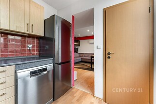 Kuchyň s moderními spotřebiči, dřevěnými skříňkami a parketovou podlahou, navazující na světlý obývací pokoj s velkými okny.