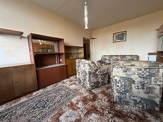 Obývací pokoj s retro kobercem, dřevěnými skříněmi a pohovkou s vintage vzorem, nabízí útulný prostor v původním stavu.