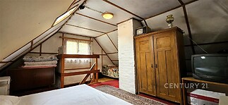 Podkrovní ložnice s dřevěným obložením, parketová podlaha, starožitná skříň, světlé okno, útulný styl.