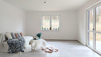 Světlý obývací pokoj s velkými okny, moderní parketová podlaha a výhledem do zahrady, minimalistický styl, útulný a prostorný interiér.