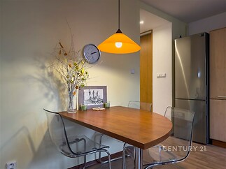 Jídelní kout s moderním dřevěným stolem, parketovou podlahou a designovým osvětlením. Elegantní kombinace skla a dřeva vytváří útulnou atmosféru.