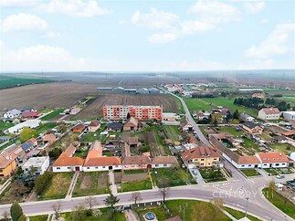 Pohled na malebnou venkovskou lokalitu s rodinnými domy, moderní stavbou a rozsáhlými poli, klidné prostředí pro bydlení