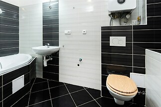 Moderní koupelna s dlažbou, závěsnou toaletou a umyvadlem. Kontrastní obklady a plynový kotel doplňují elegantní vzhled.