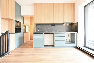 Moderní kuchyň s parketovou podlahou, dřevěnými skříňkami a velkým oknem. Kombinace šedých a přírodních tónů vytváří elegantní vzhled.