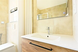 Moderní koupelna s dlažbou, dřevěnou skříňkou a velkým zrcadlem, elegantní design a světlé provedení vytváří příjemné prostředí.