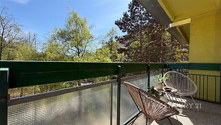 Prostorný balkon s výhledem na zeleň, moderní kovové zábradlí, pohodlná venkovní sezení, slunná orientace.