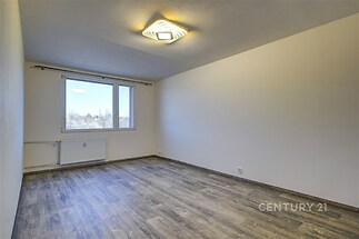 Prázdný světlý pokoj s parketovou podlahou, velkým oknem a moderním osvětlením, vhodný pro obývací pokoj v rekonstruovaném bytě.