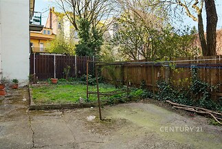 Zahrada s dlážděnou plochou a trávníkem, ohraničená dřevěným plotem. Nachází se zde vzrostlé stromy a keře, ideální soukromí pro relaxaci.