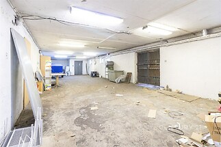 Průmyslový sklad s betonovou podlahou, kovovými vraty a zářivkami, vhodný pro rekonstrukci nebo skladování.