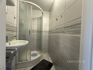 Moderní koupelna s dlažbou, sprchovým koutem a umyvadlem. Světlé keramické obklady dodávají prostoru elegantní vzhled.