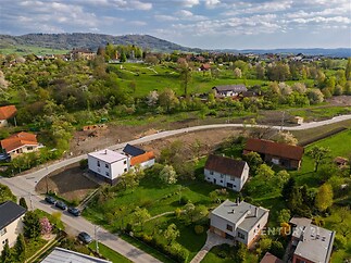 Rodinné domy na klidném předměstí s upravenou zelení, velkými zahradami a malebným výhledem na okolní krajinu, vhodné pro rodinné bydlení.