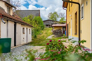 Atraktivní venkovský dvůr s dlážděnou cestou, dřevěnou kůlnou a udržovanou zahradou, ideální pro milovníky klidu a přírody.
