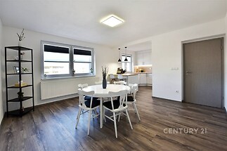 Světlá jídelna s moderní parketovou podlahou, velká okna, bílý nábytek, přímý přístup do kuchyně, stylový interiér.