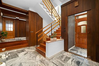Vstupní hala s mramorovou dlažbou, dřevěným obložením a schodištěm s dřevěnými zábradlím, nabízí elegantní a útulný design.
