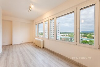 Světlý obývací pokoj s velkými okny, moderní laminátovou podlahou a výhledem na okolí, nabízí prostorný a útulný interiér.