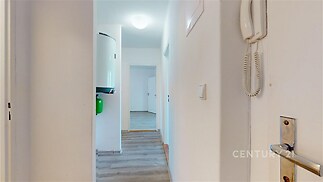 Úzká chodba s laminátovou podlahou, moderním osvětlením a vestavěným bojlerem, vede k dalším pokojům v rekonstruovaném bytě.