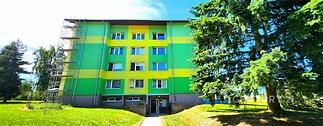 Zrekonstruovaný panelový dům s barevnou fasádou v klidné lokalitě obklopený zelení, nabízí prostorné bytové jednotky s moderními prvky.