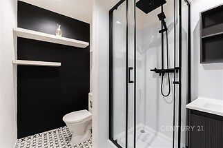 Moderní koupelna s proskleným sprchovým koutem, černobílými dlaždicemi a stylovými úložnými policemi vytváří elegantní a sofistikovaný prostor.