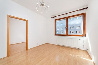 Světlý obývací pokoj s parketovou podlahou, velkým oknem a moderními svítidly. Propojeno s další místností, nově rekonstruováno.
