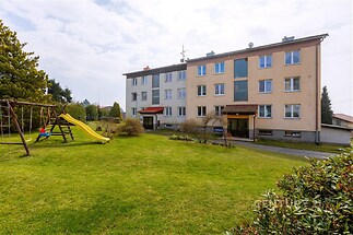 Bytový dům s dobře udržovaným trávníkem, dětským hřištěm a vzrostlými stromy, klidná lokalita, ideální pro rodiny.