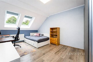 Podkrovní ložnice s parketovou podlahou a střešními okny, moderní design, komoda z dřeva a pracovní stolek, světlý a vzdušný prostor.