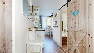 Úzká chodba s dřevěnými dveřmi a parketovou podlahou, vedoucí do světlé kuchyně s velkým oknem a moderním vybavením.