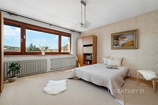 Prostorná ložnice s velkými okny, světlý koberec a vestavěné skříně, moderní dekor s výhledem na okolní krajinu.