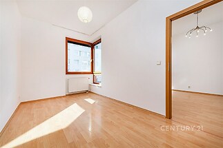 Světlý obývací pokoj s parketovou podlahou a velkými okny, moderní design a neutrální stěny umožňují personalizaci prostoru.
