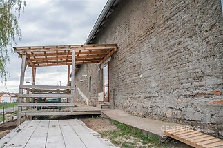 Venkovní terasa s dřevěnou pergolou a betonovou cestou, vedle zdi s venkovským vzhledem, ideální pro relaxaci na zahradě.