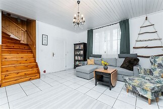 Světlý obývací pokoj s dlažbou, velká okna propouštějící přirozené světlo, moderní vybavení, dřevěné schodiště dodává útulnou atmosféru.