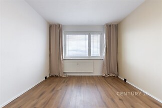 Prázdný pokoj s dřevěnou podlahou, velkým plastovým oknem a světlými stěnami, vhodný pro flexibilní uspořádání interiéru.