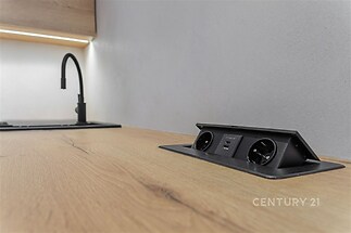 Moderní kuchyň s dřevěnou pracovní deskou, vestavěné elektrické zásuvky a USB porty, minimalistická černá armatura, elegantní design.