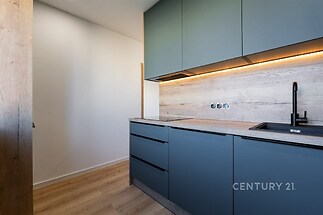 Moderní kuchyň s dřevěnou podlahou, vestavěné skříně, minimalistický design, LED osvětlení pod skříněmi, matné povrchy, elegantní černý dřez.
