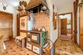 Rustikální kuchyň s dlažbou a kachlovými kamny, dřevěné obložení, tradiční dekorace, světlé stěny a historický stylový interiér.
