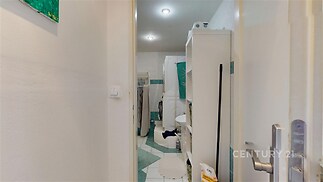 Úzká koupelna s dlažbou, bílé skříňky, světlé stěny, v rohu pračka, dobře udržovaná, útulná a praktická dispozice