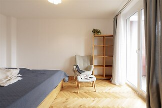 Prostorná ložnice s parketovou podlahou, velká okna zajišťují světlý prostor, moderní nábytek nabízí pohodlí a stylovou atmosféru.